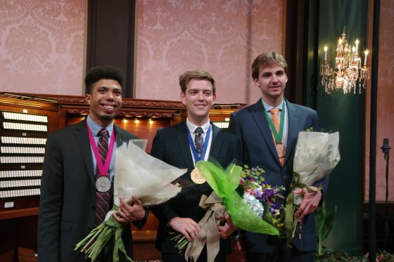Three people holding bouquets of flowers standing in front of an organ.
